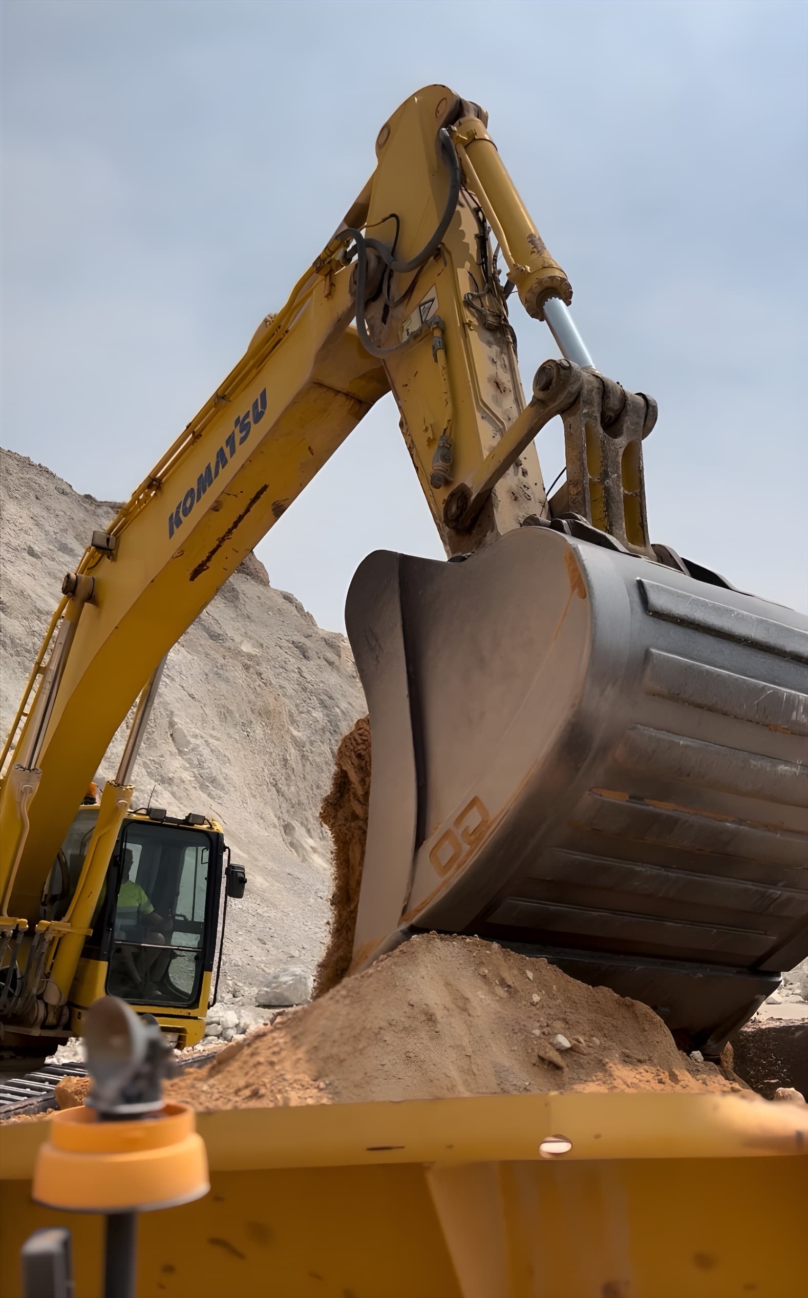 Excavadora amarilla Komatsu moviendo tierra con su gran cuchara metálica en una cantera soleada.